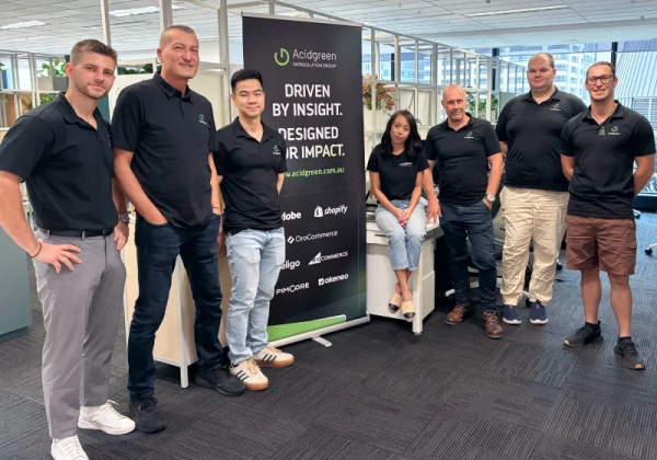 Acidgreen's Australian team stands alongside a branded banner inside their Sydney office.