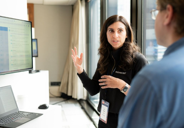 A Mimecast employee discusses their cloud solutions with a client, referencing their desktop.